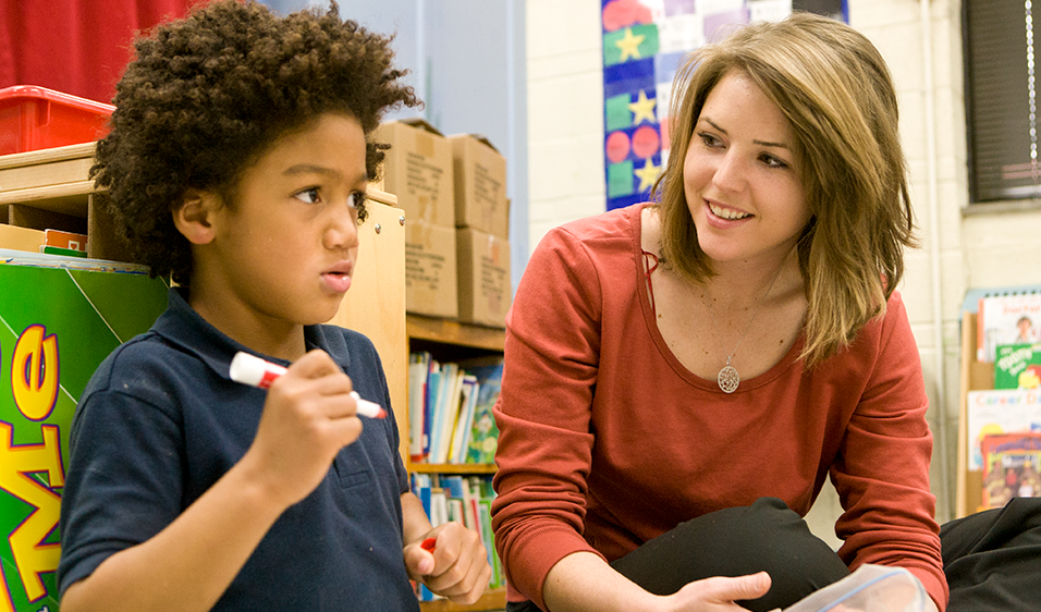 Female student helping with young male kid in an education setting.